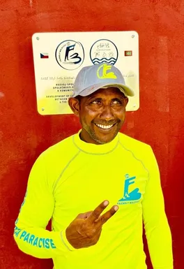 Místní obyvatel pózuje s úsměvem před pamětní plaketou symbolizující spolupráci Friendly Maldives a komunity rybářů na ostrově Gemanafushi